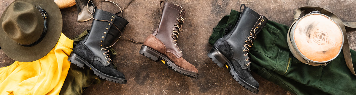 Three tall leather wildland fire boots in black and brown arranged on a rustic floor with forest service gear