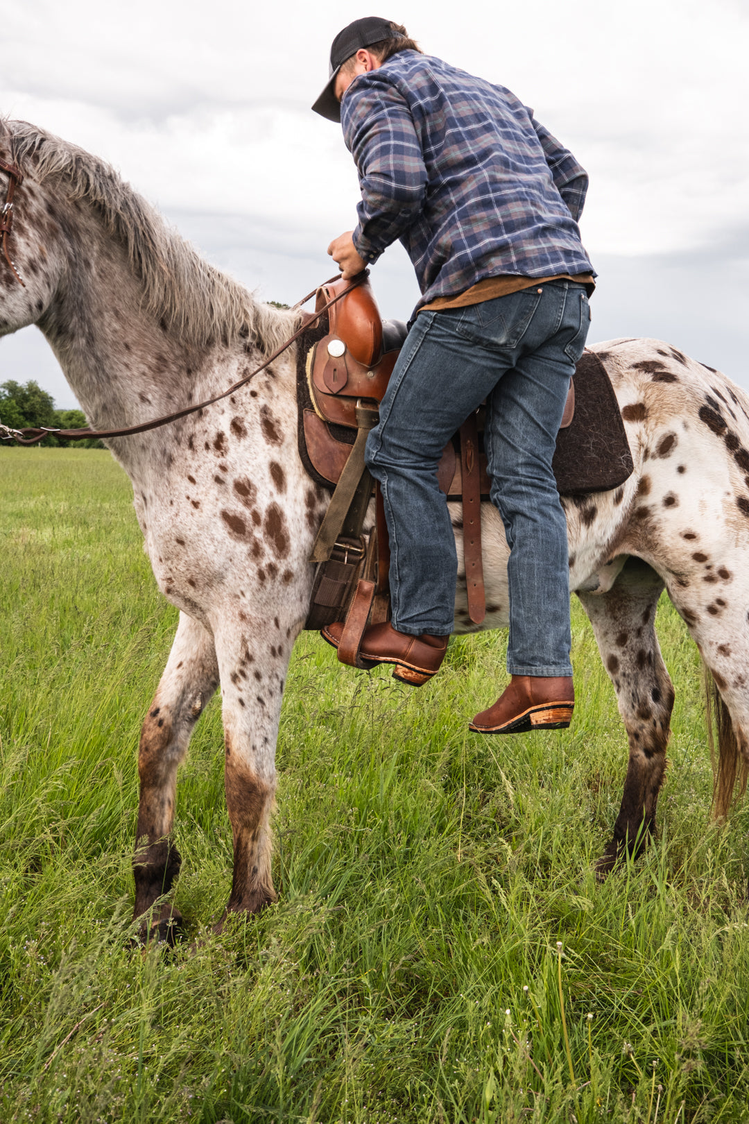 Man riding a spotted horse wearing brown leather western boots in a grassy field