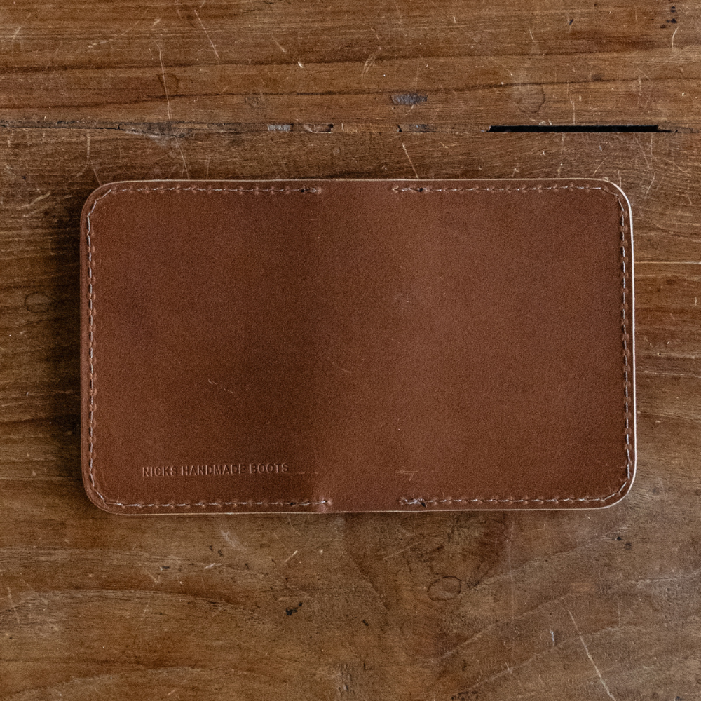 Brown leather Heritage Calf Wallet with perimeter stitching lying flat on a wooden surface