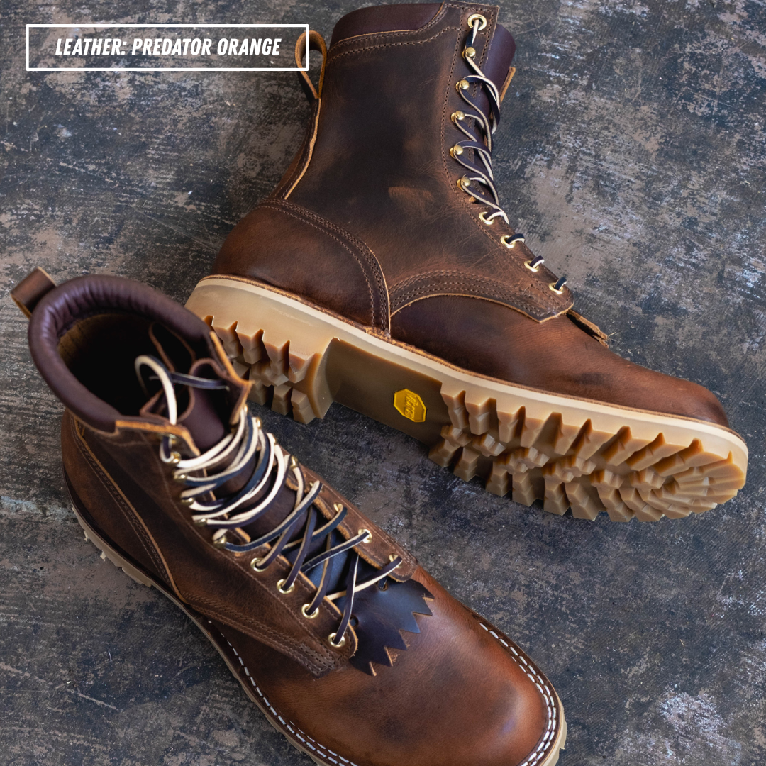 Two rugged lace-up boots in distressed brown leather, one upright and one angled to show the sole, placed on a dark textured surface. A text label in the top left reads 'LEATHER: PREDATOR ORANGE'.