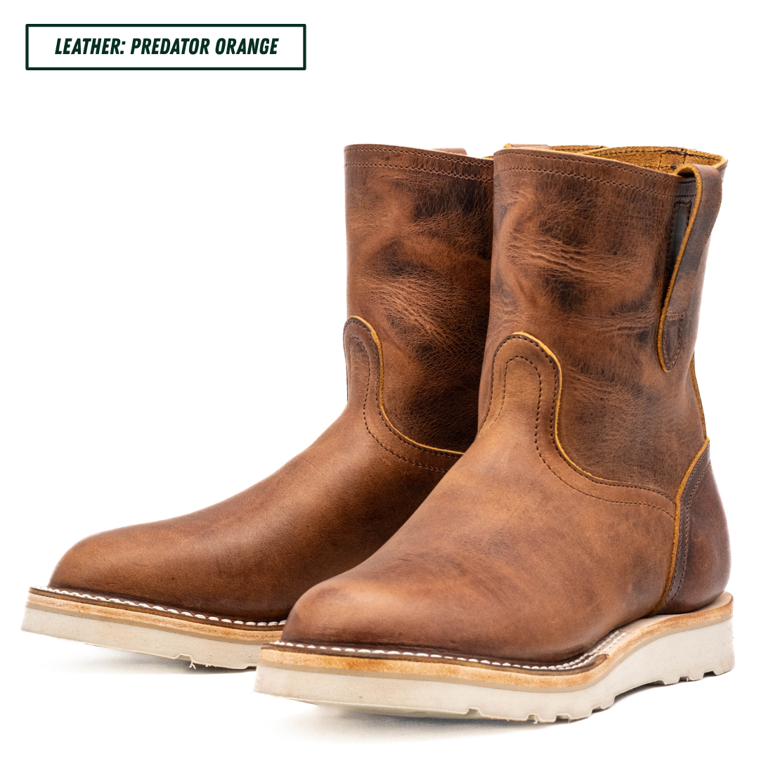 A pair of distressed brown leather ankle boots with a western design, featuring a pull-on style toe and thick off-white soles. A text label in the top left corner reads 'LEATHER: PREDATOR ORANGE'.