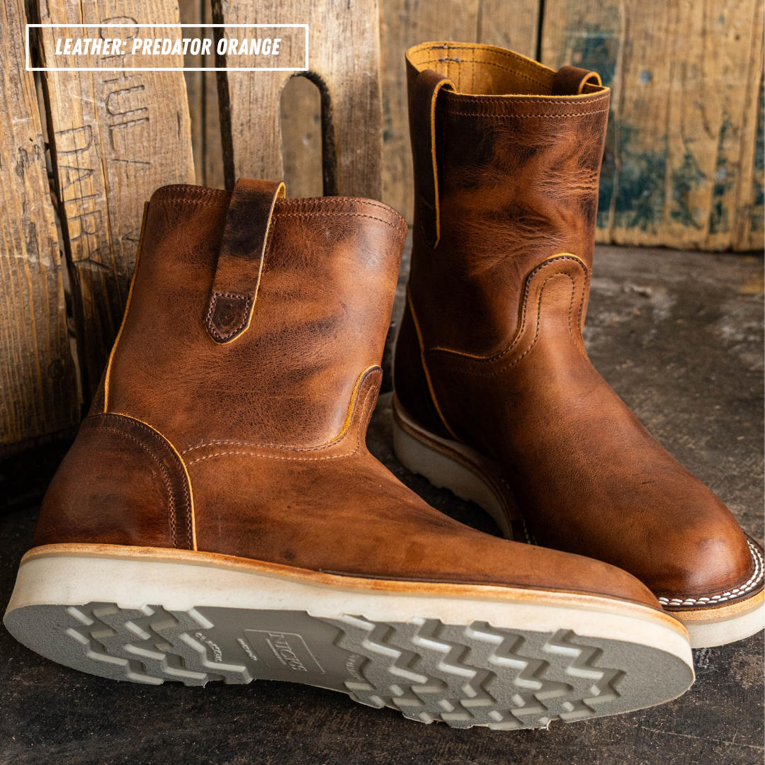 A pair of distressed brown leather mid-calf boots with yellow stitching, shown on a dark rustic surface with wooden planks in the background. A text overlay in the top left reads 'LEATHER: PREDATOR ORANGE'.