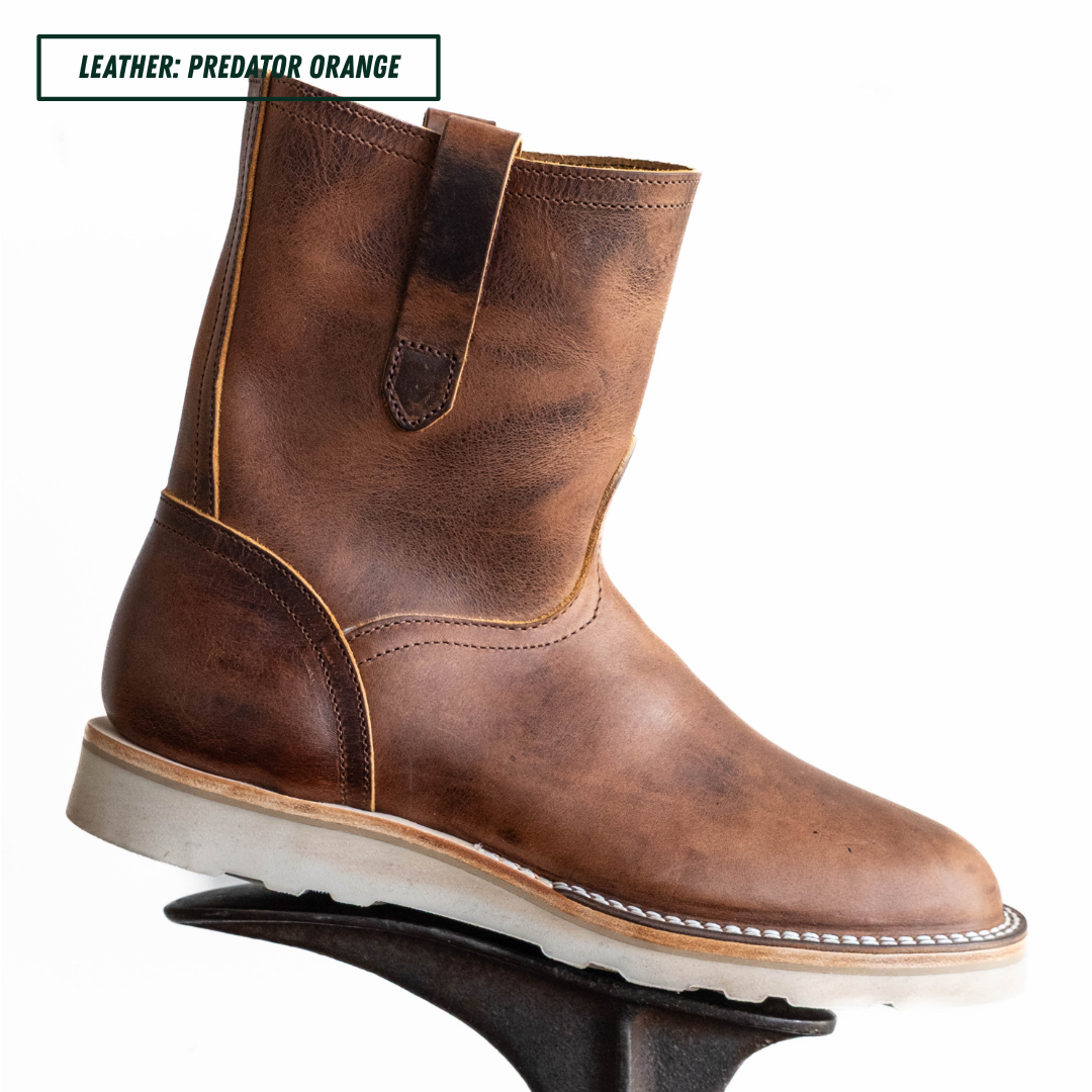 A brown leather ankle boot with a pull strap and white sole, shown on a black display stand against a white background. A text label in the top left reads 'LEATHER: PREDATOR ORANGE'.