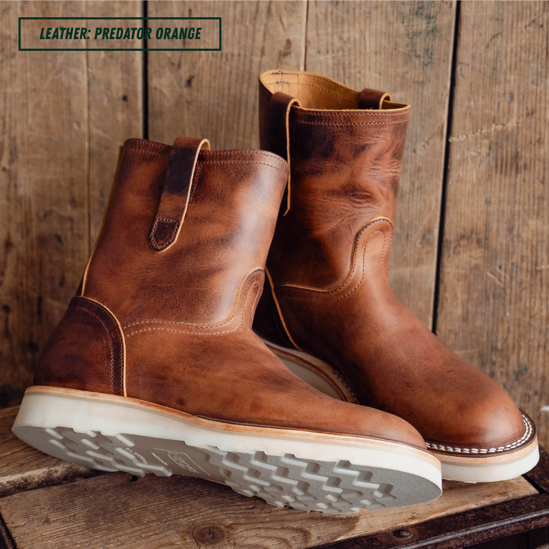 A pair of mid-calf leather boots in a distressed brown shade, displayed on a rustic wooden surface against a wooden plank background. A text overlay in the top left corner reads 'LEATHER: PREDATOR ORANGE'.