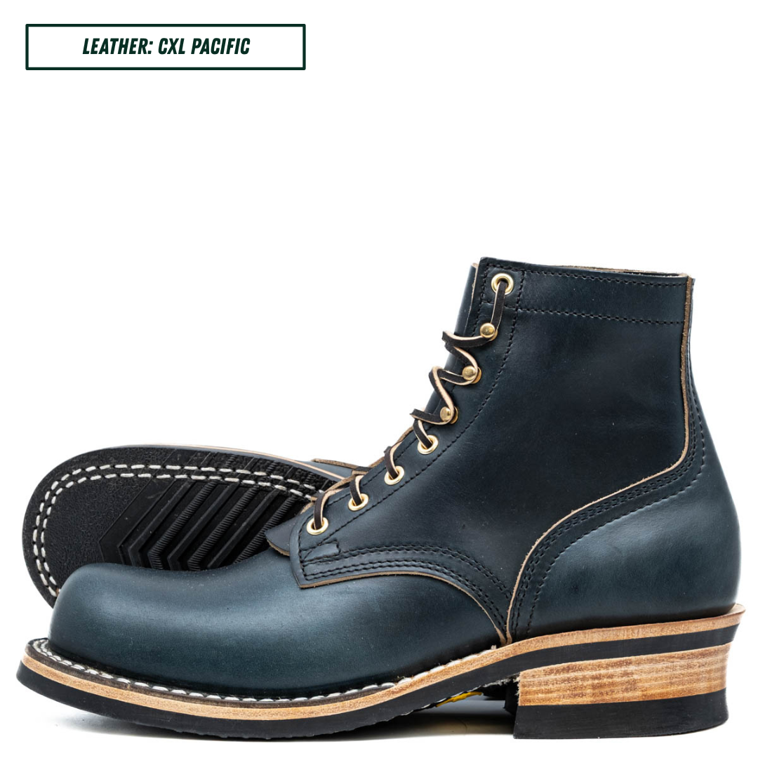 A pair of dark navy blue leather lace-up ankle boots with light tan stitching, gold eyelets, and stacked wood-look heels, shown on a white background with a text label in the top left corner.