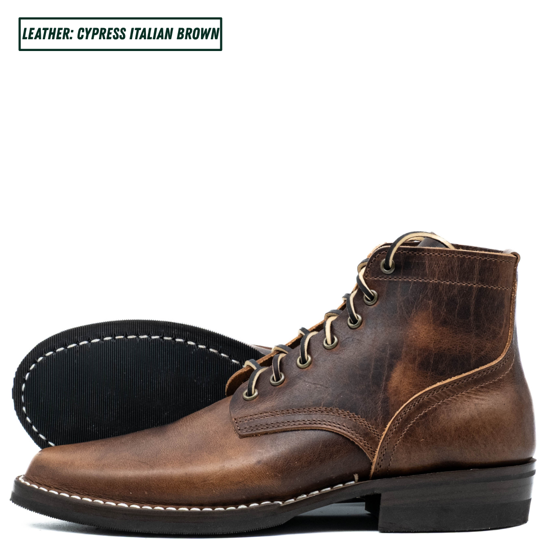 A single lace-up ankle boot in distressed brown leather, shown in side profile with the outsole visible behind it on a white background. A small label in the top left reads 'LEATHER - CYPRESS ITALIAN BROWN'.