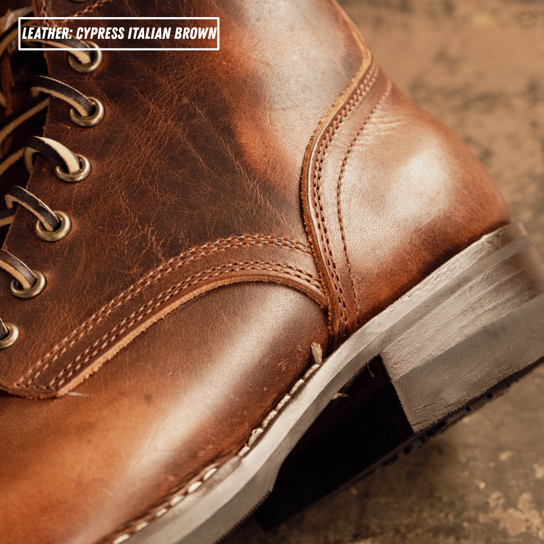 Close-up of a brown leather lace-up boot showing the side panel, stitching, eyelets, and part of the sole, with text reading 'LEATHER - CYPRESS ITALIAN BROWN'.