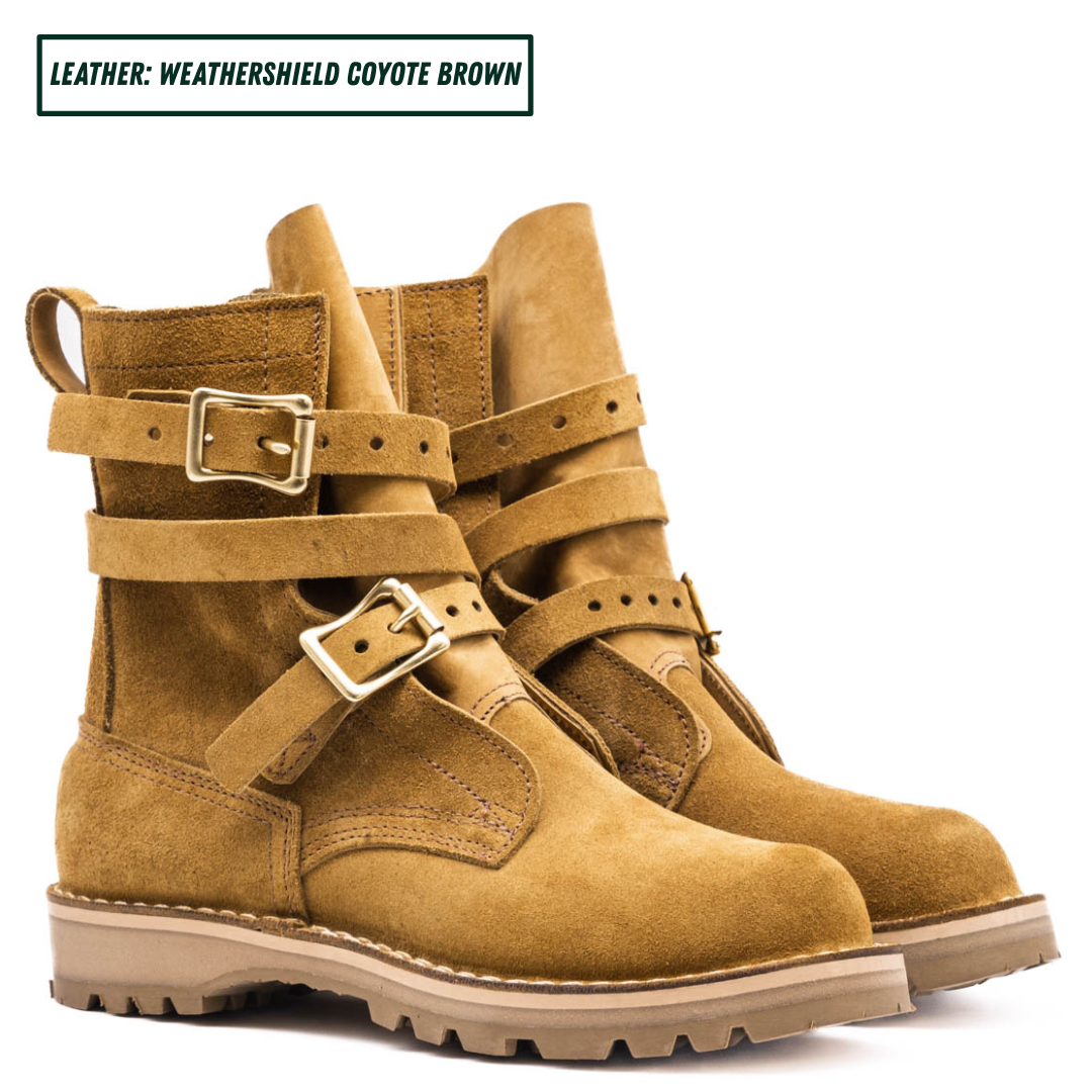 A pair of mid-calf boots in a warm coyote brown suede-like leather, featuring double buckle straps on the sides and a rugged lug sole. Boots sitting together facing forward right.
