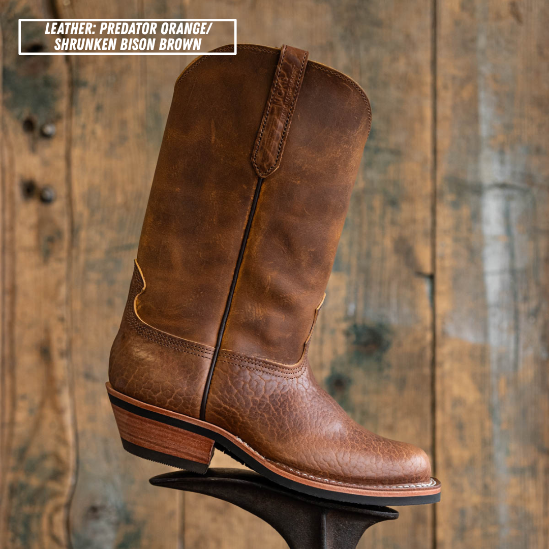 A single brown leather cowboy boot with a distressed finish, shown standing on a display stand against a rustic wooden plank background. A text overlay in the top-left corner reads 'LEATHER: PREDATOR ORANGE / SHRUNKEN BISON BROWN'.