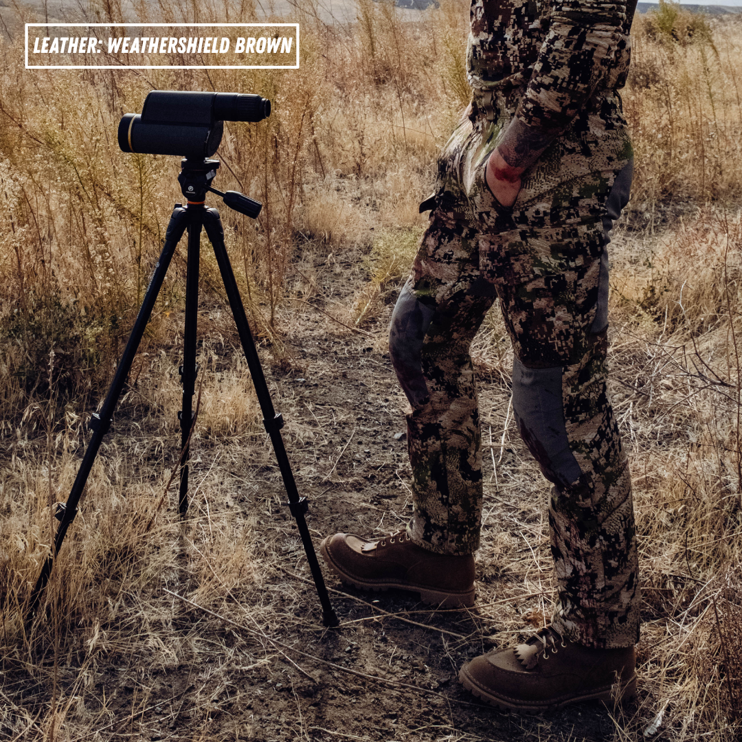 A person in camouflage outdoor clothing stands beside a black binocular mounted on a tripod in a dry grassy field. A text box in the top left reads 'LEATHER: WEATHERSHIELD BROWN'.