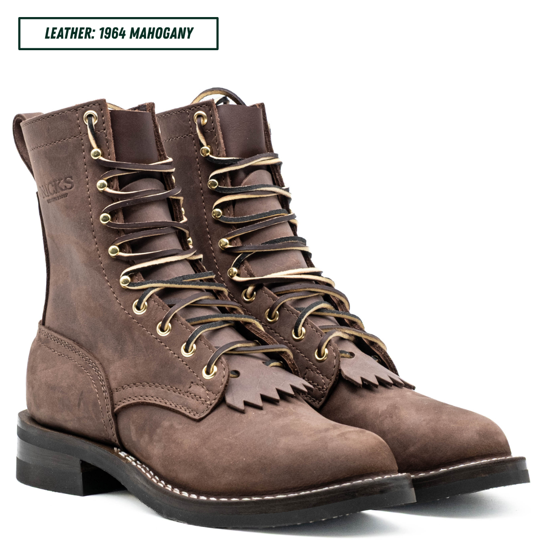A pair of brown suede lace-up boots with gold-toned eyelets and fringe detail on the vamp, shown on a white background with a text label reading 'LEATHER: 1964 MAHOGANY'.