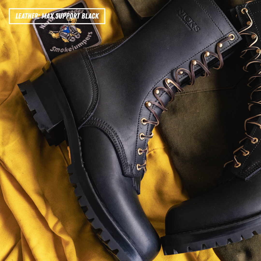 A pair of black leather lace-up boots with dark brown laces and brass eyelets, displayed on a draped yellow fabric background. A black patch with a blue logo and the text 'Smokejumpers' is visible in the top-left corner.