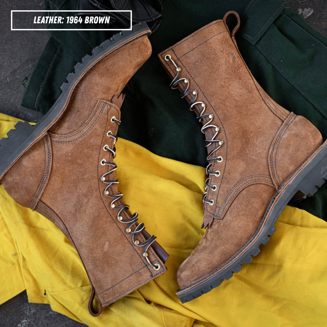 A pair of lace-up ankle boots in distressed brown leather, arranged on a bright yellow fabric with dark green pants in the background. A text overlay in the top-left corner reads 'LEATHER: 1964 BROWN'.