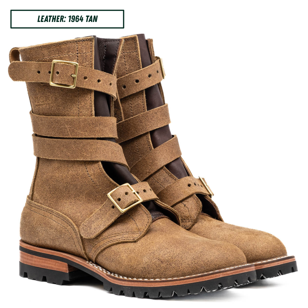 A pair of mid-calf leather boots in tan leather with multiple wrap-around straps and brass-tone buckles, shown on a white background with a small label reading 'LEATHER: 1964 TAN'.