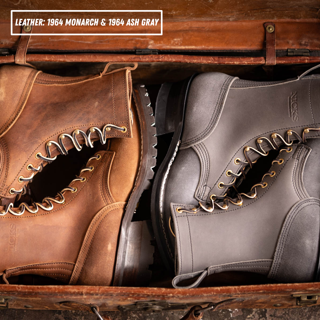 Two work boots displayed inside an open leather trunk: a brown boot on the left and an ash gray boot on the right. Text at the top reads 'LEATHER: 1964 MONARCH & 1964 ASH GRAY'.