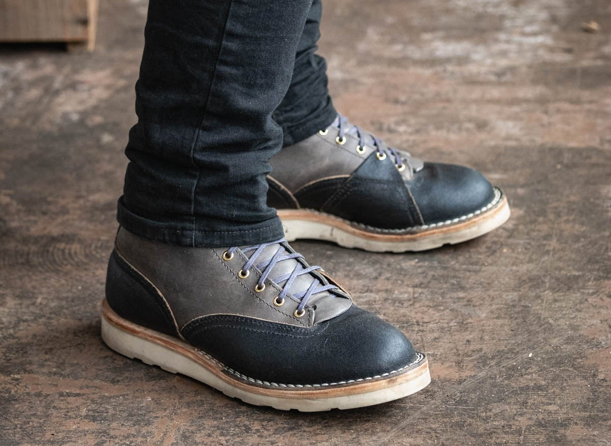Person wearing dark blue leather shoes with white soles on a wooden floor.