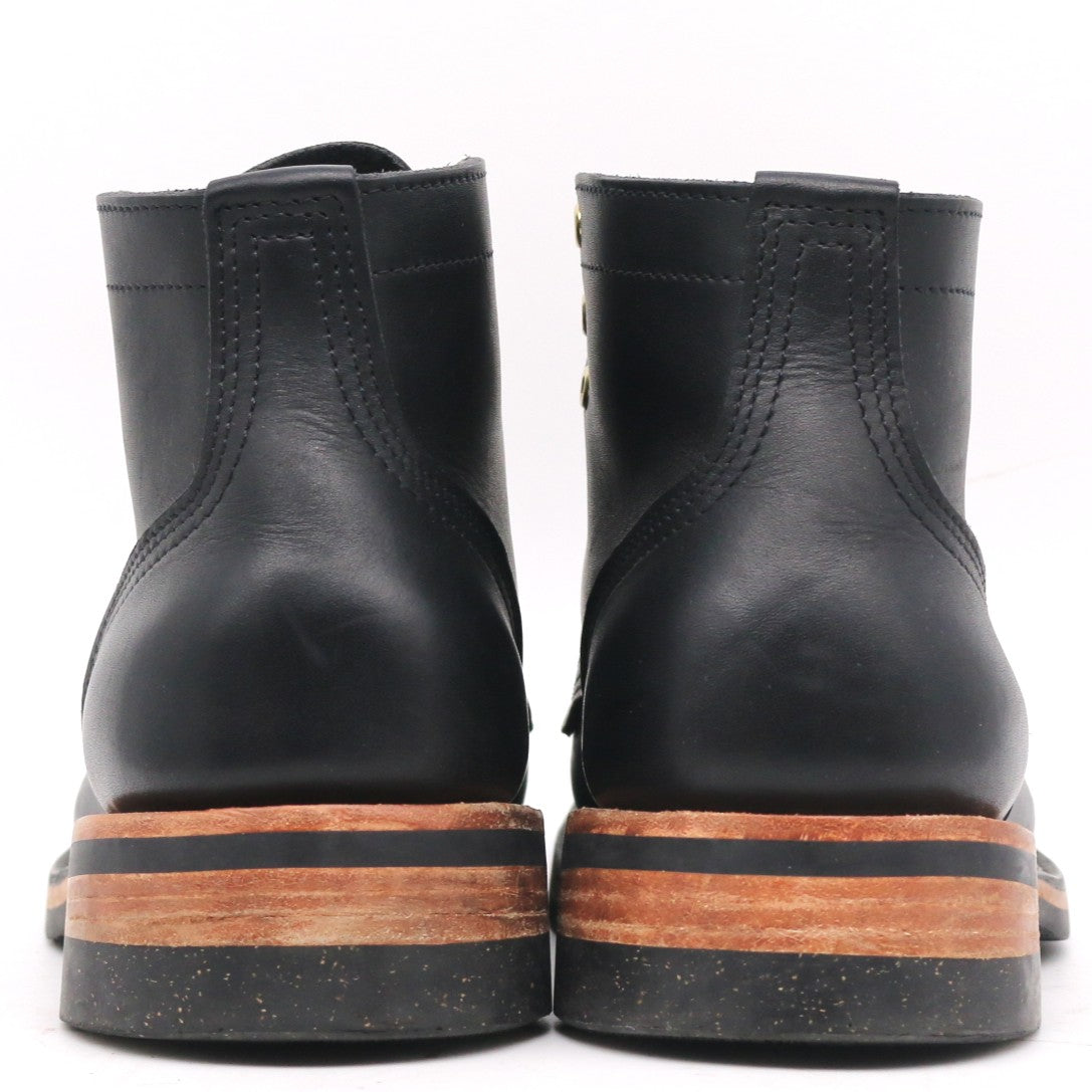 A pair of black leather ankle boots shown from the back, featuring a stacked sole with a brown wood-look layer and a black rubber outsole, set against a plain white background.