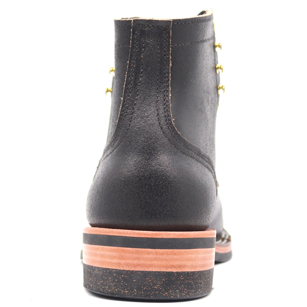A black leather ankle boot shown from the back, featuring a stacked sole with a black rubber top, a tan mid-layer, and a dark speckled base, accented by gold-tone eyelets.