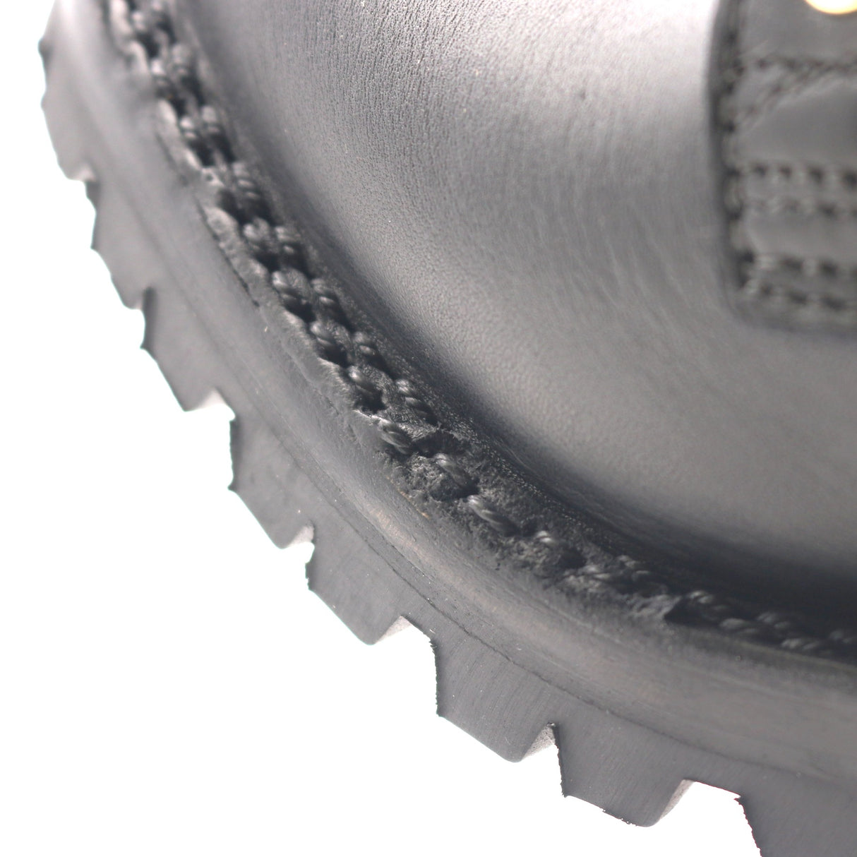 Close-up of a black leather boot corner showing the stitched welt, textured sole edge, and part of the heel on a white background.