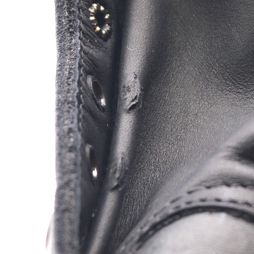 Close-up of a black leather boot showing the side profile with metal eyelets and a small tear or scuff on the leather surface.