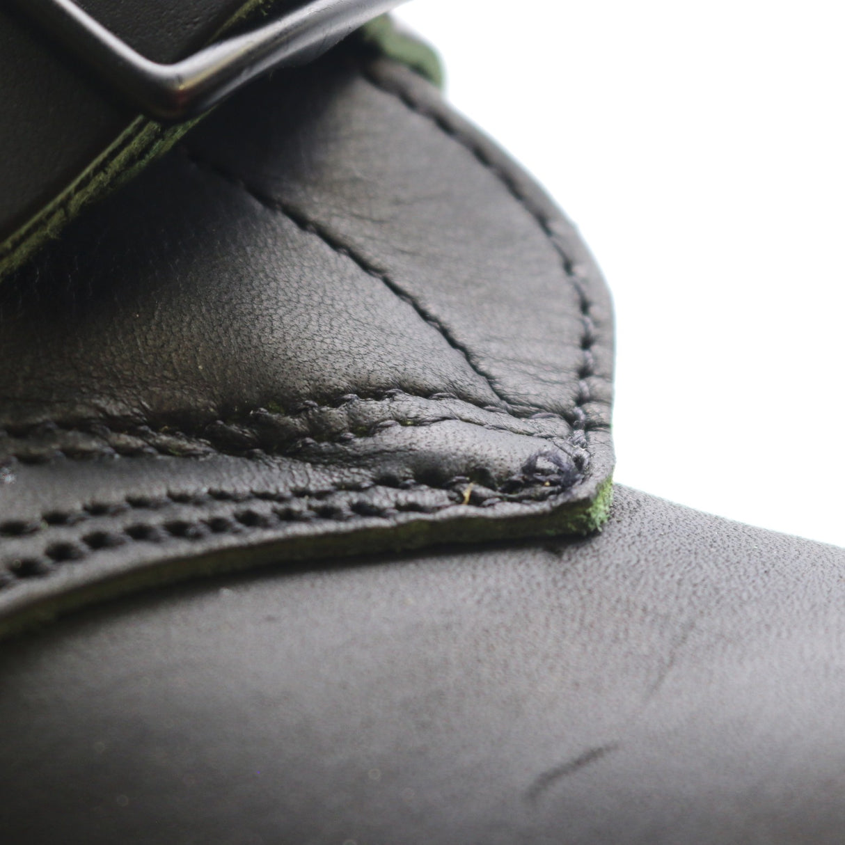 Close-up detail of a black leather strap or belt with visible stitching and a metal buckle, set against a bright white background.