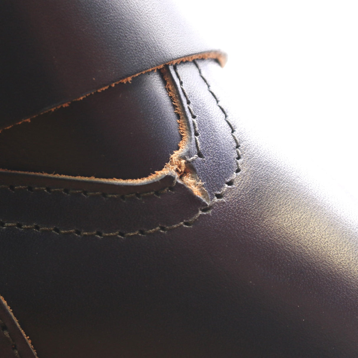 Close-up of a dark brown leather boot showing a stitched leather detail with the edge of the leather slightly worn and exposed.