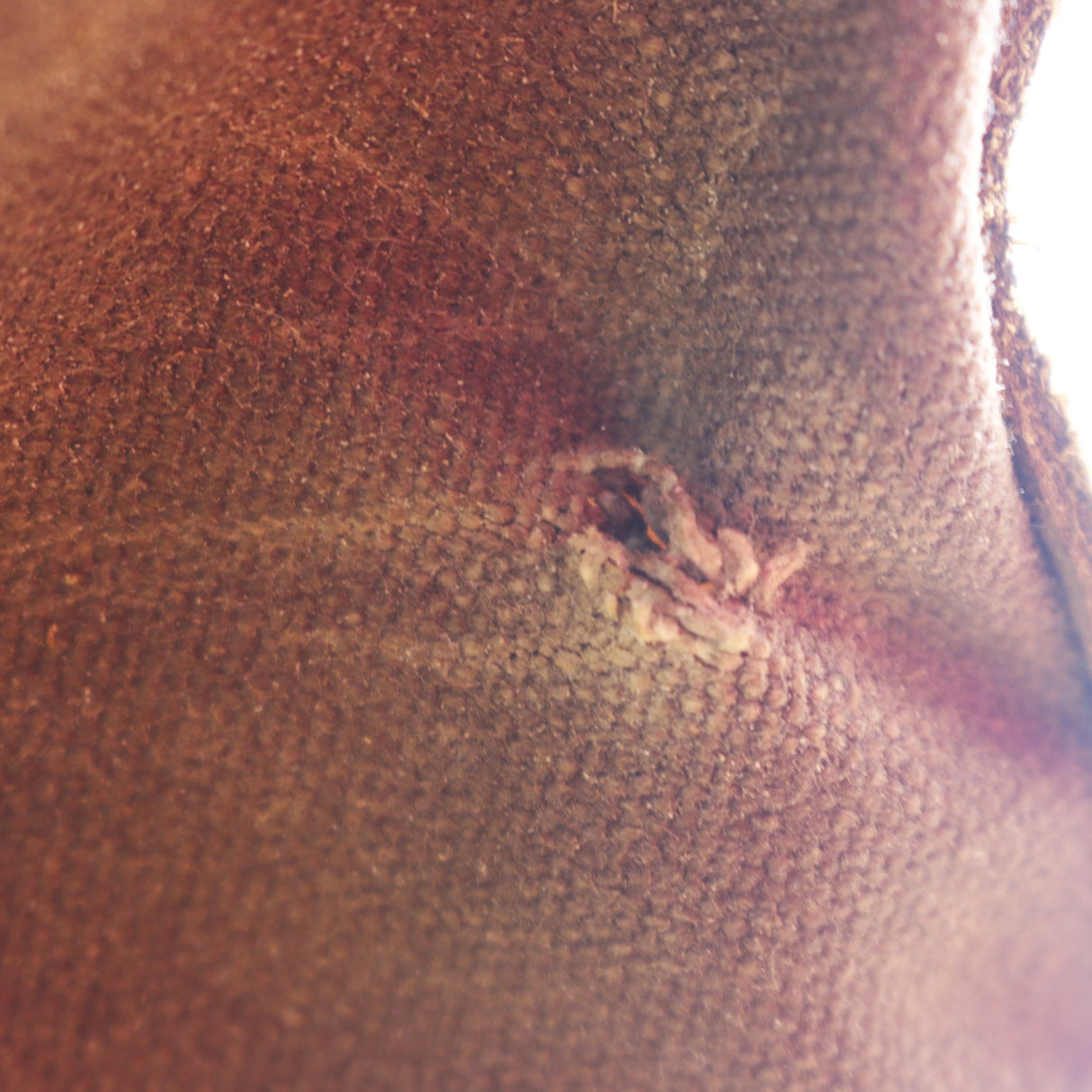 A close-up shot of a textured brown leather or faux-leather surface with a small, distressed tear or scuff near the center.