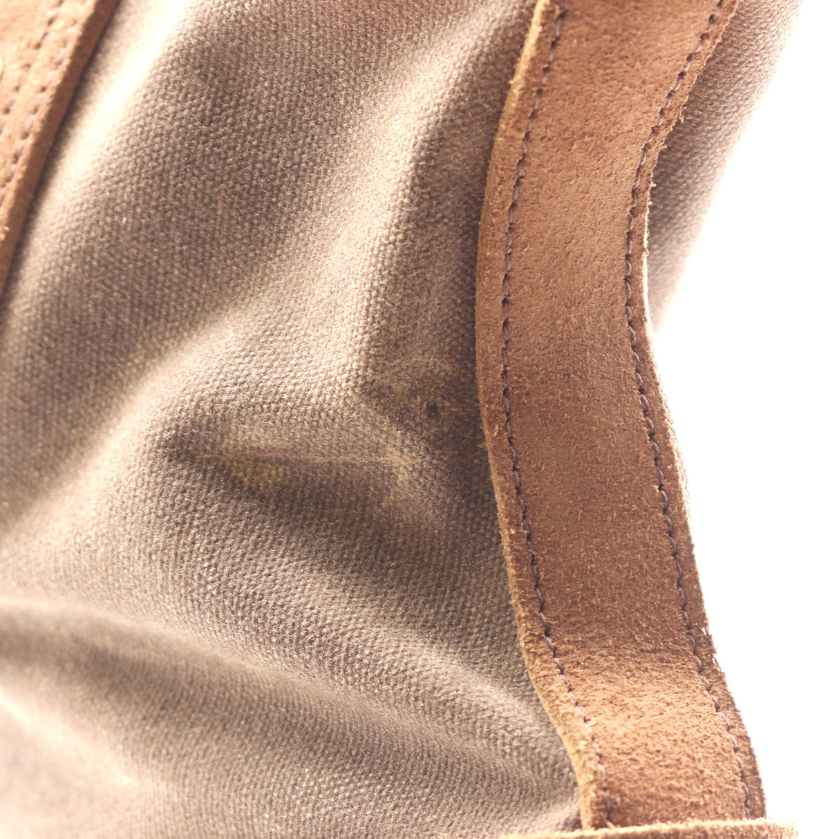 Close-up detail of a canvas bag showing a taupe-brown canvas body and a contrasting tan suede strap with matching stitching.