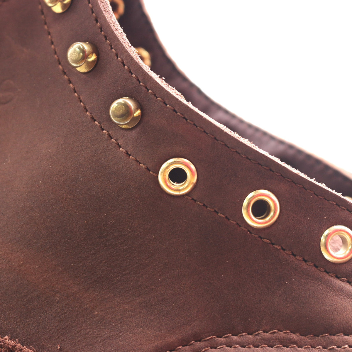 Close-up of a dark brown leather boot or shoe upper with brass eyelets and matching metal rivets along the collar.