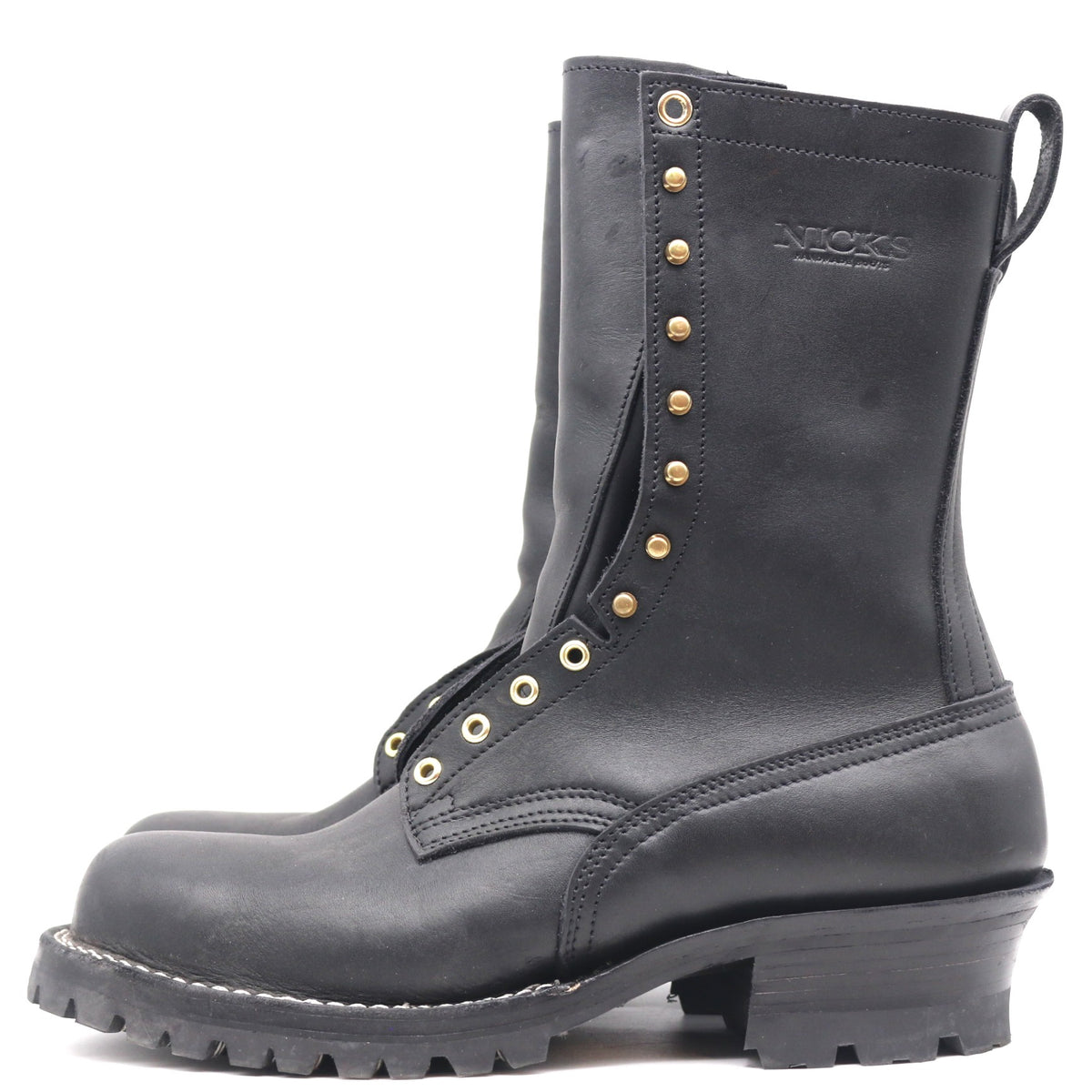 A black leather work boot with gold-tone metal eyelets, studs, and a pull tab, shown from a side profile on a white background. The brand name 'NICKS' is embossed on the side.