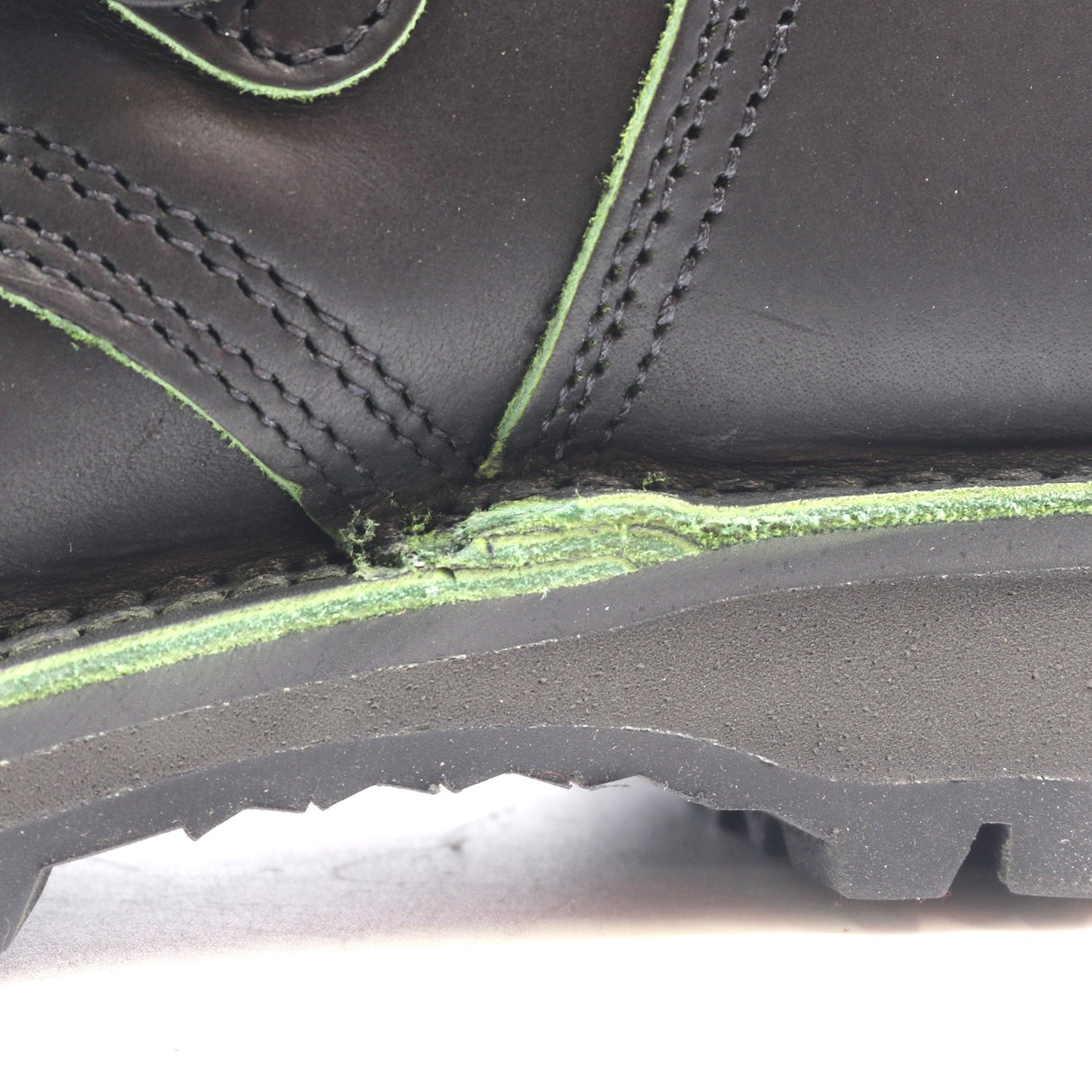 Close-up of a black leather boot showing a heavily worn, frayed, and damaged green sole edge.