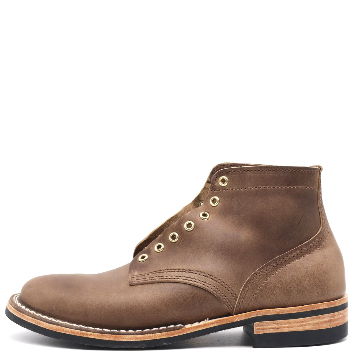 A brown leather lace-up ankle boot with brass eyelets, white contrast stitching, and a stacked black and tan sole, shown from a side profile on a white background.