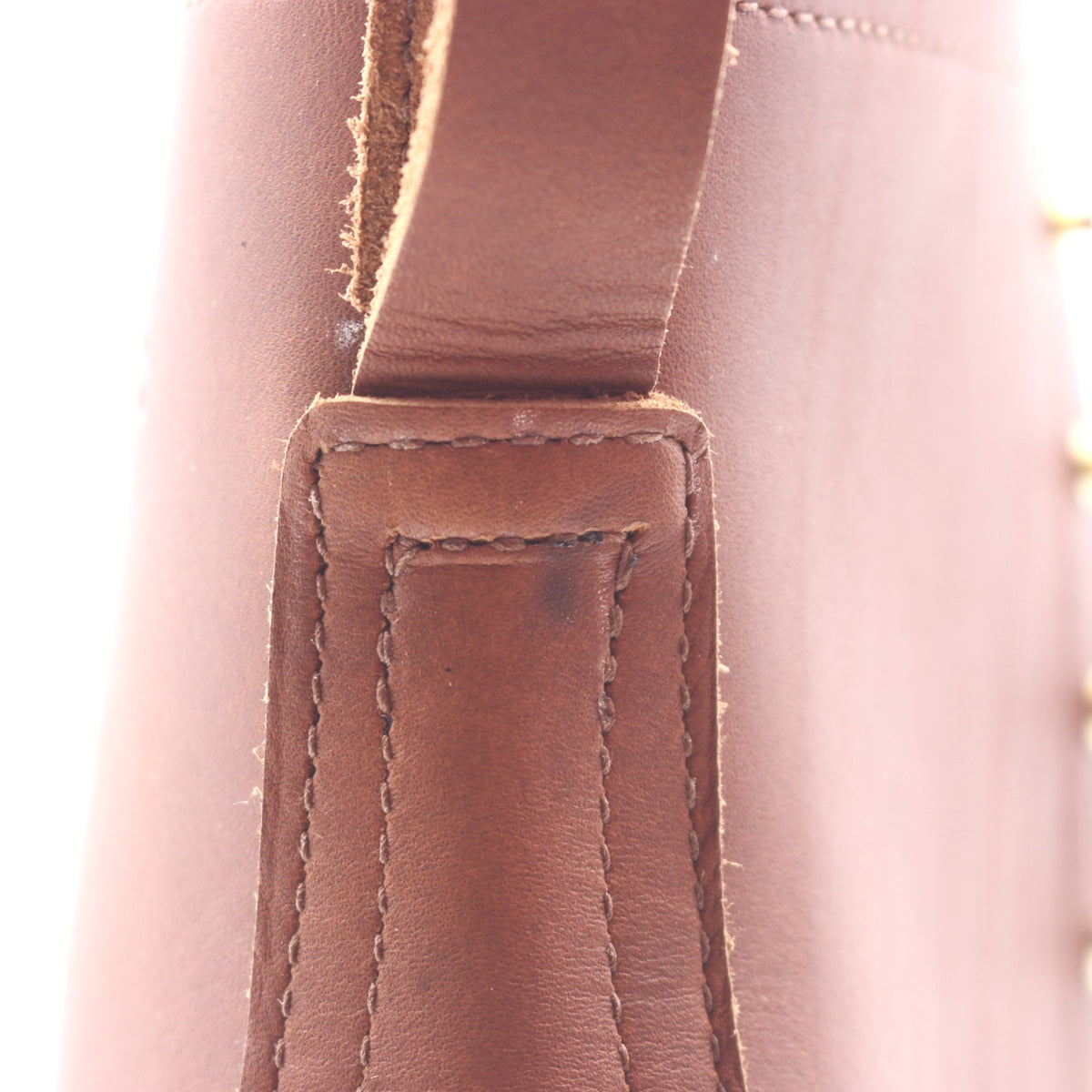Close-up detail of a brown leather strap and stitched leather tab on a boot. Visible scorch mark under the pull loop.