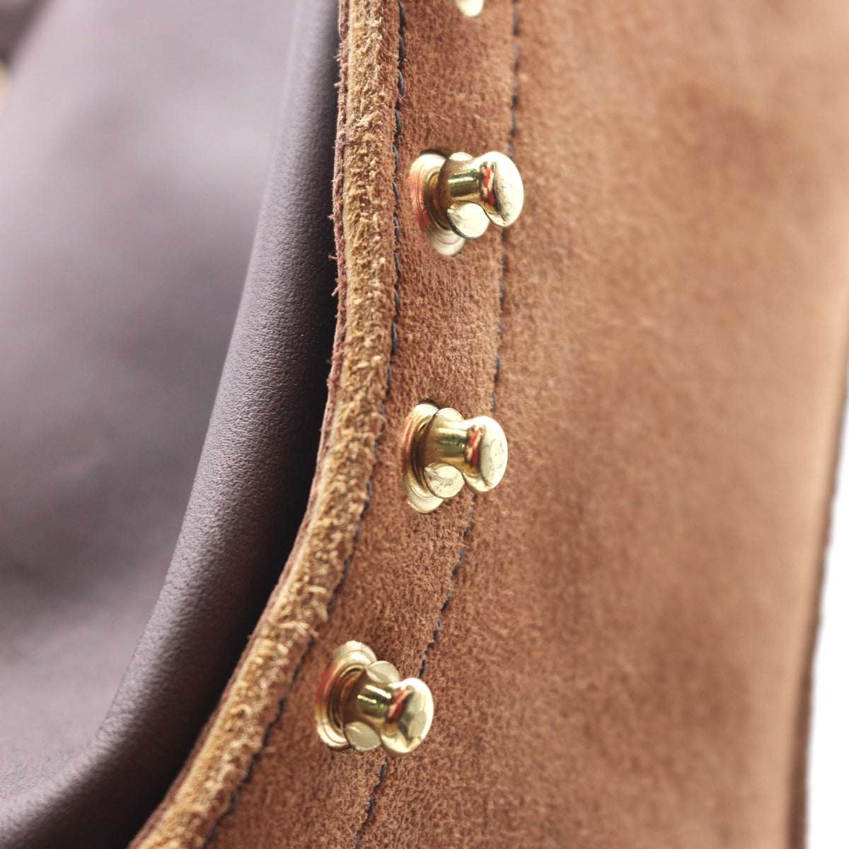 Close-up detail of a brown suede or leather strap with brass-tone rivets and a dark brown inner lining.