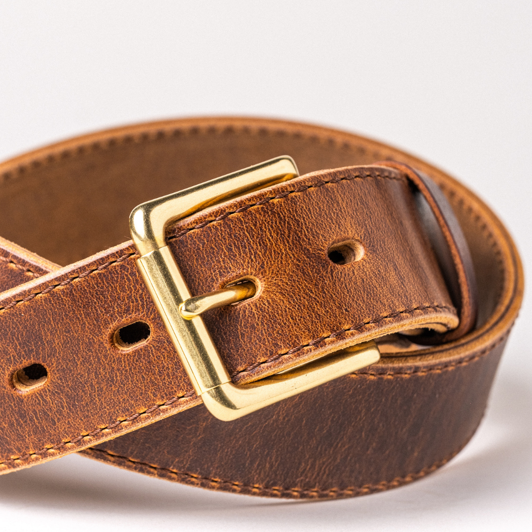 A close-up of a brown leather belt with a gold-tone buckle, coiled on a light gray background.