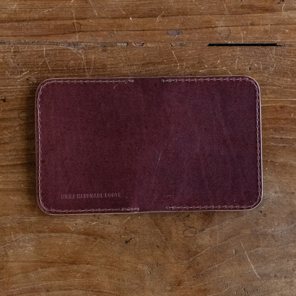 Burgundy leather Heritage Calf Wallet with perimeter stitching lying flat on a wooden surface
