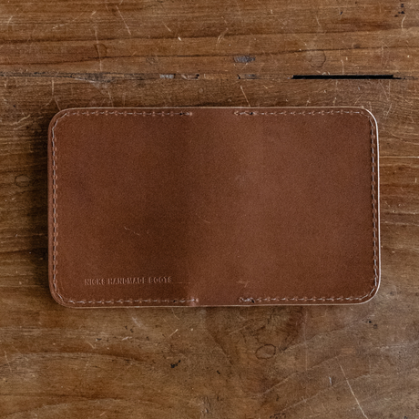 Brown leather Heritage Calf Wallet with perimeter stitching lying flat on a wooden surface