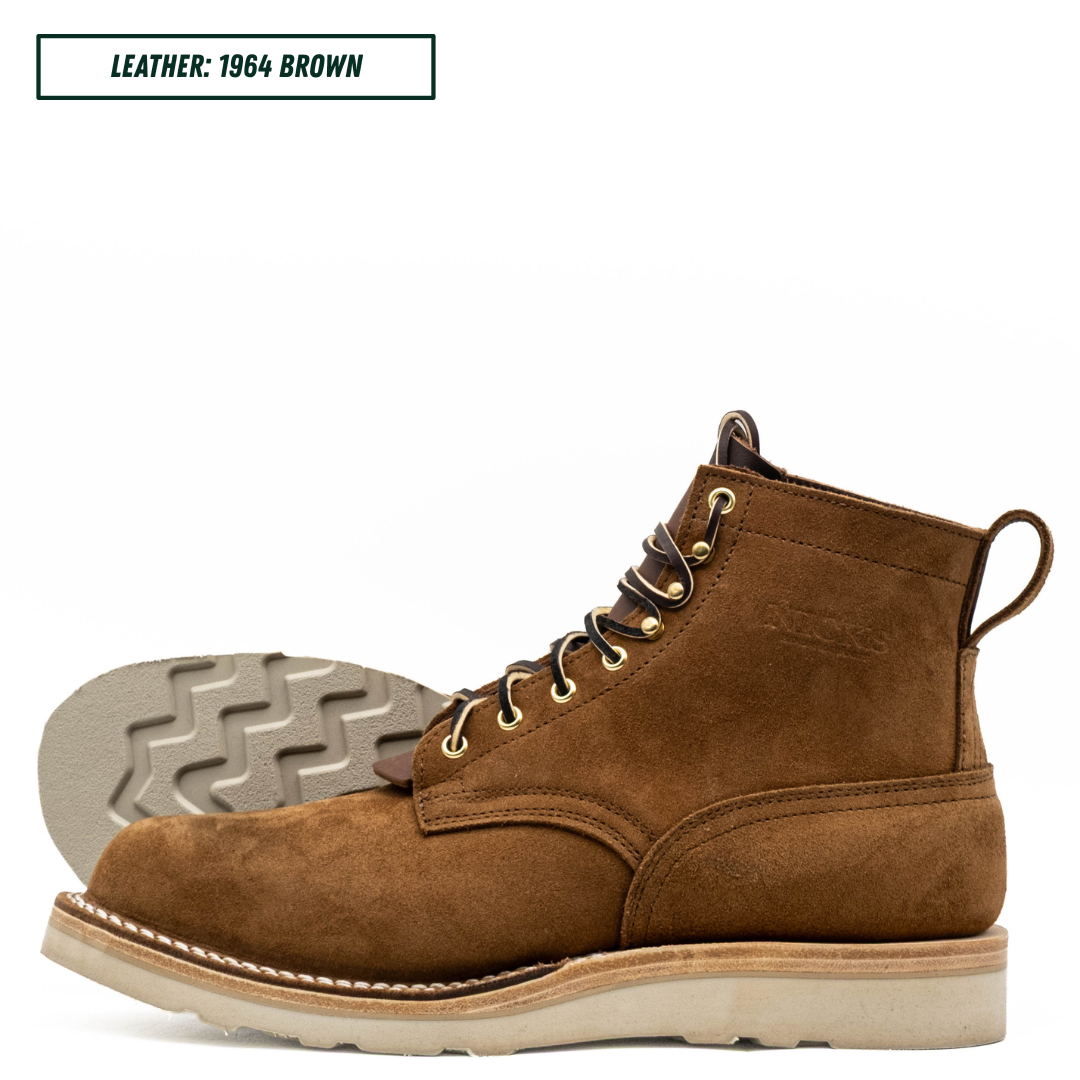 A single brown suede lace-up boot shown in side profile on a white background, with the outsole visible behind it. A small text label at the top reads 'LEATHER: 1964 BROWN'.