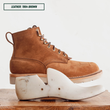 A brown suede lace-up ankle boot shown in side profile on a boot jack, with a 55 last on a wooden surface below and a text label reading 'LEATHER: 1964 BROWN' in the top left.