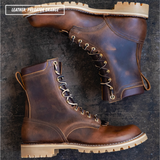 A pair of rugged lace-up work boots in distressed brown leather with tan soles, arranged on a dark textured surface. A text overlay in the top-left corner reads 'LEATHER: PREDATOR ORANGE'.