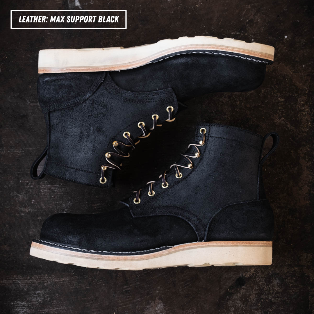 Short black boots laying on textured concrete. Top left reads "LEATHER: MAX SUPPORT BLACK."