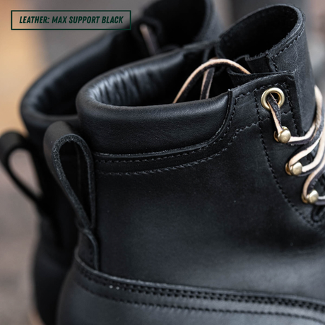 Close-up of a black leather lace-up boot with metal eyelets and white laces, showing the ankle collar and pull tab, with a text label reading 'LEATHER: MAX SUPPORT BLACK' in the top-left corner.