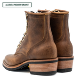 A pair of distressed brown leather lace-up ankle boots with stacked wood-look heels, shown from a three-quarter rear angle on a white background. A text label in the top-left corner reads 'LEATHER: PREDATOR ORANGE'.