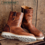 A pair of mid-calf leather boots in a distressed brown shade, displayed on a rustic wooden surface against a wooden plank background. A text overlay in the top left corner reads 'LEATHER: PREDATOR ORANGE'.