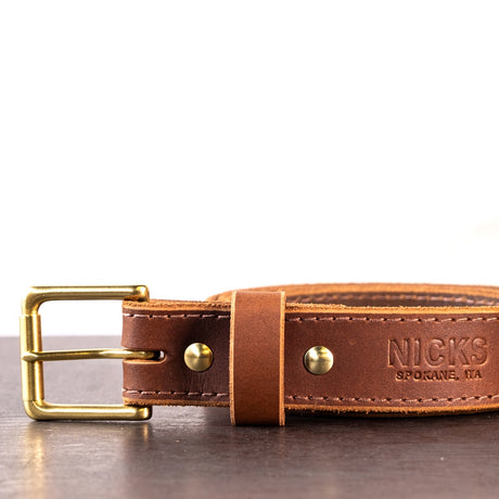 Brown belt with brown stitching and brass hardware sitting on metal surface