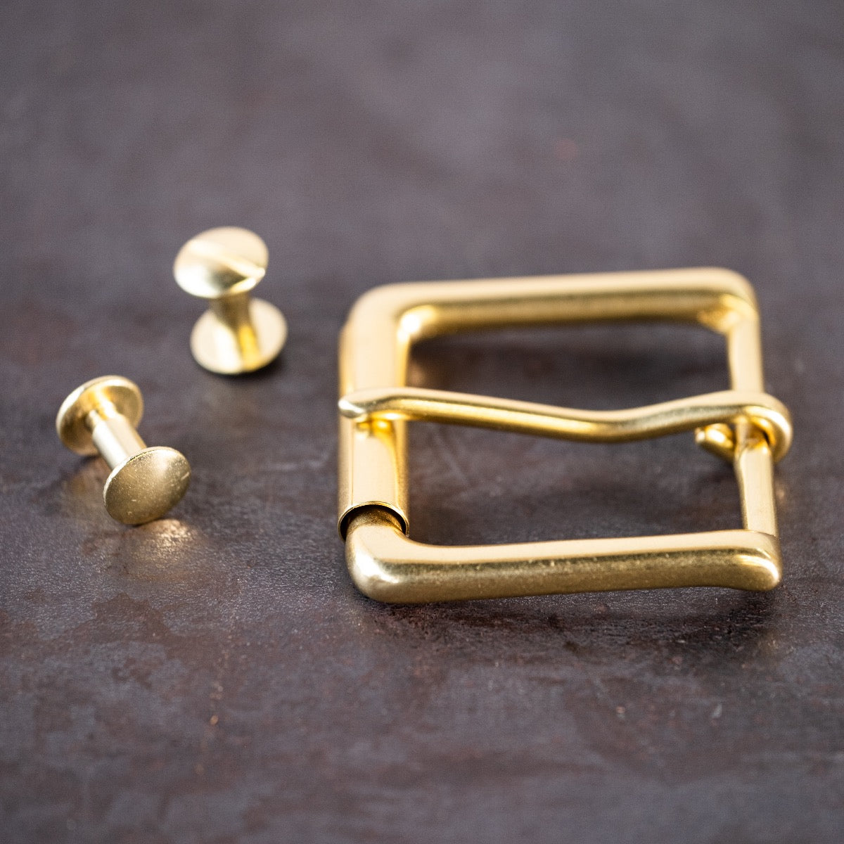 Brass belt buckle and brass Chicago screws sitting on a metal surface