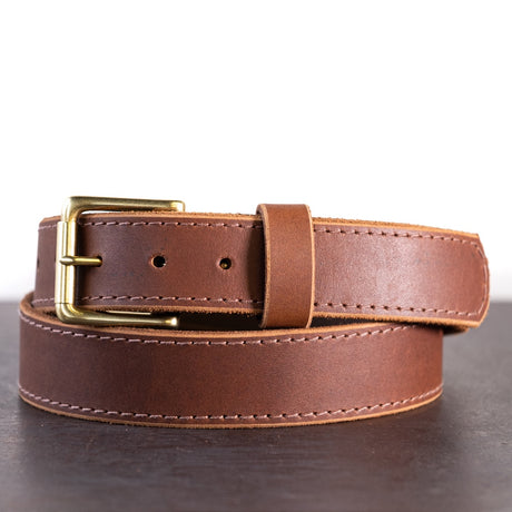 Brown belt with brown stitching and brass hardware sitting on metal surface with white background