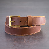 Brown belt with brown stitching and brass hardware sitting on metal surface