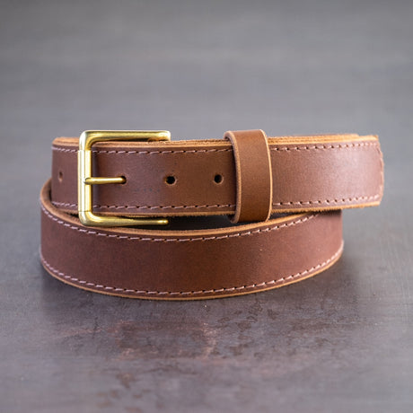 Brown belt with brown stitching and brass hardware sitting on metal surface