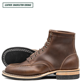 A pair of rich brown lace-up ankle boots in Shackleton Cognac, with one boot standing upright and the other lying on its side to show the treaded sole. A text label in the top left reads 'LEATHER: SHACKLETON COGNAC'.